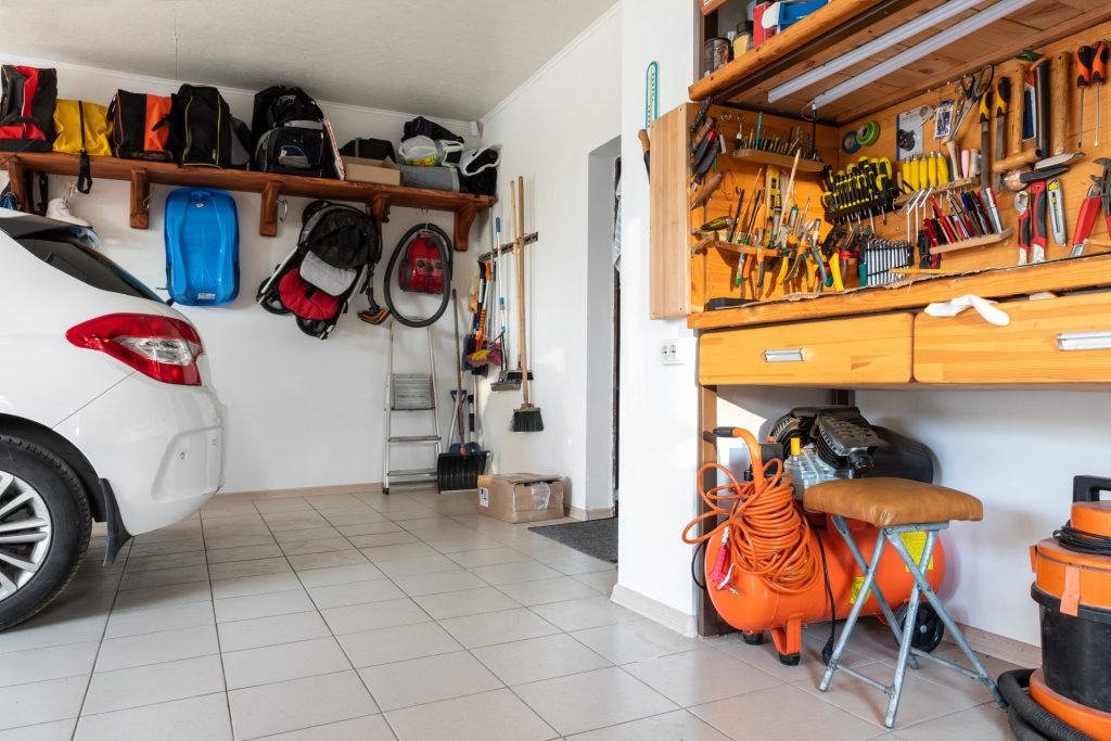 Residential garage with a parked car, organized tools, storage shelves, and workshop equipment.